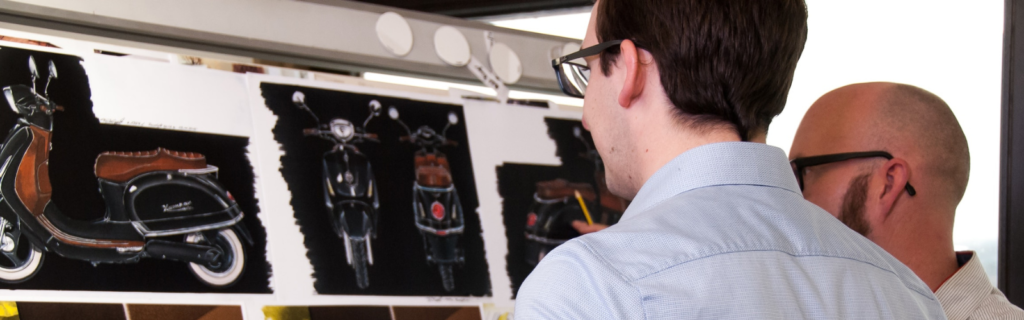 Two men standing in front of computer monitors looking at product designs on screen.